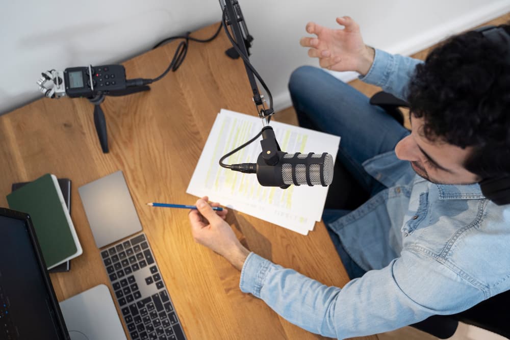 Creator at a desk with a studio microphone, laptop, and marked-up video scripts