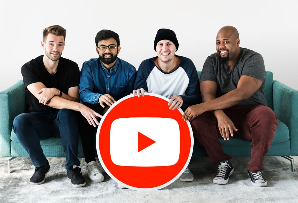 Four people sitting together holding a large YouTube play-button icon